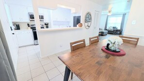 Une cuisine moderne avec des meubles blancs, un coin repas doté d’une table en bois, et un salon avec un canapé et une table basse.