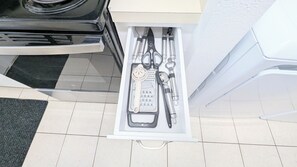 A drawer with various kitchen utensils including a grater, scissors, and a bottle opener.
