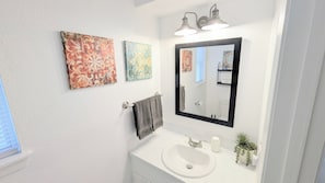 A bathroom with a white sink, a mirror, and three wall-mounted artworks.