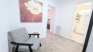 A room with a grey sofa, a large flower painting, a radiator, and a doorway leading to a bathroom.