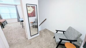 A room with a grey armchair, a small wooden table, a mirror, a staircase, and a window with blinds. - Sleep 6•Pet Friendly•Fully Stocked in East Bernard (East Bernard)