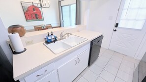A kitchen with a white countertop, a sink, a dishwashing machine, and a mirror above the sink. - Sleep 6•Pet Friendly•Fully Stocked in East Bernard (East Bernard)