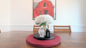 Uma mesa de jantar com um vaso de flores brancas, saleiro e pimenteiro e um jogo americano vermelho.
