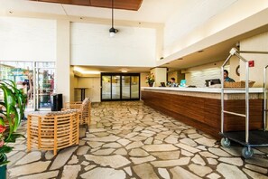 Eine Lobby mit Steinfußboden, Holzsesseln, einem Empfangstresen und einem Rollwagen.