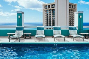 Ein Poolbereich mit Liegestühlen und Blick aufs Meer.
