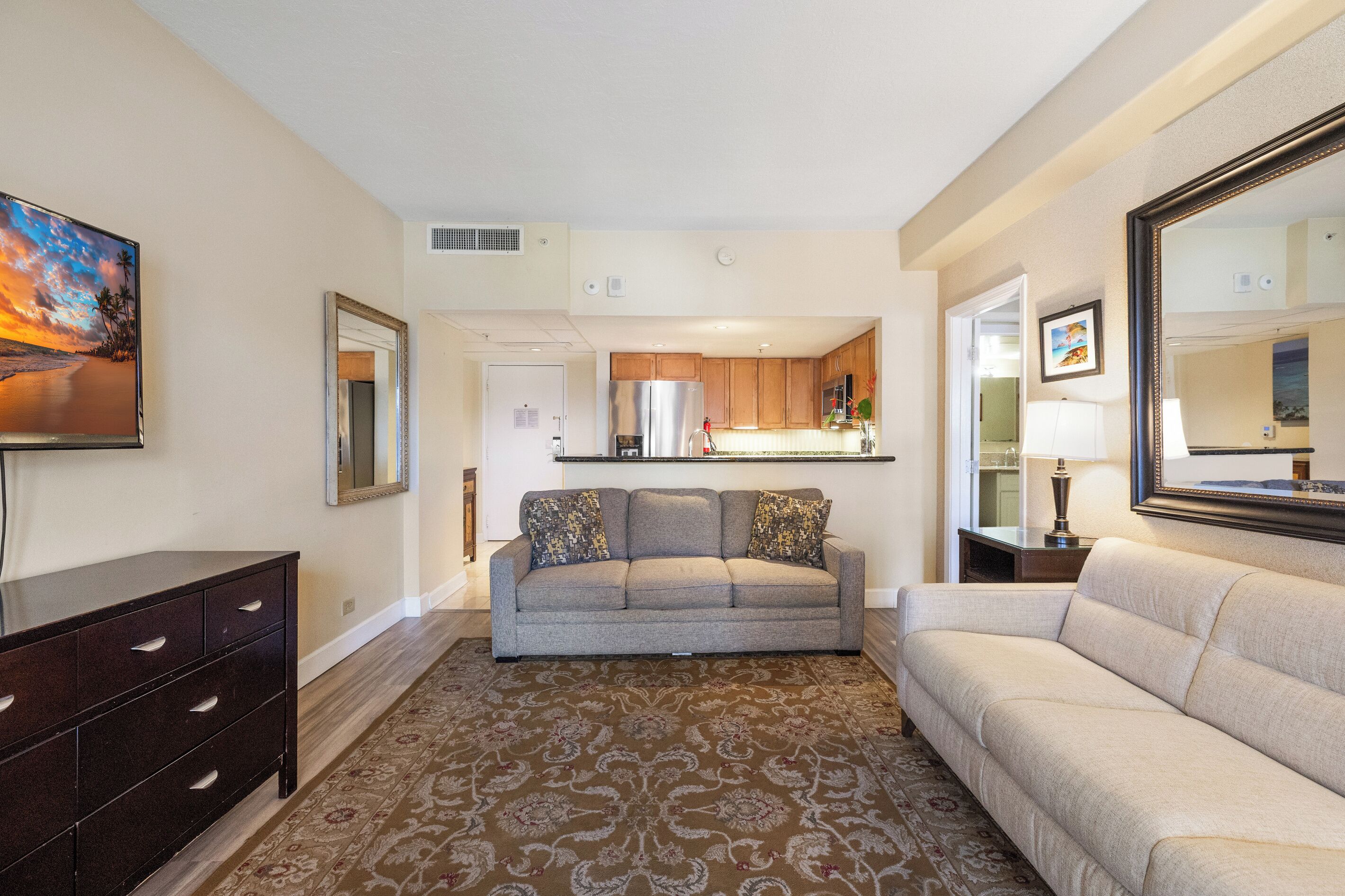 A living room with a sofa, a TV, a dresser, and a kitchen in the background.