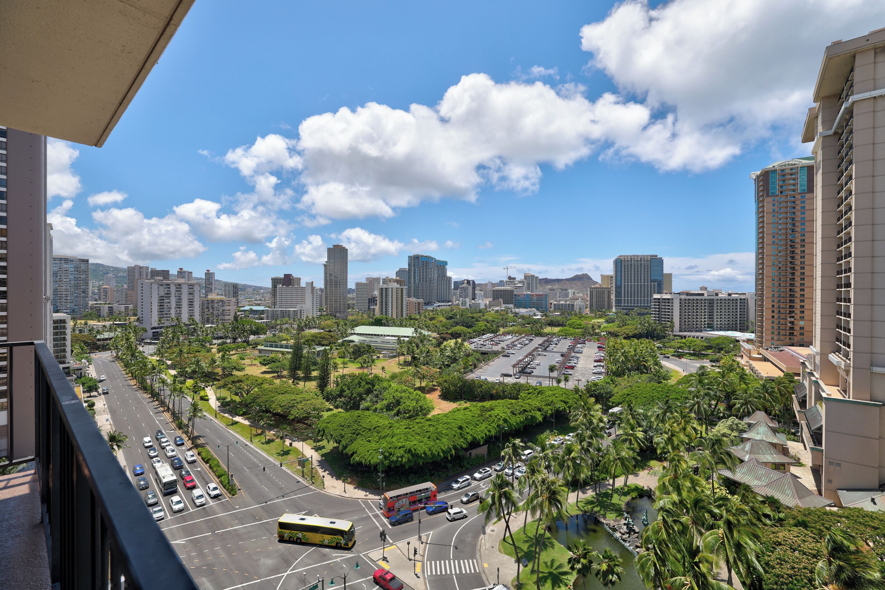 A cityscape with high-rise buildings, a parking lot, and a green park area.