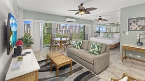 A modern living room with a sofa, coffee table, and TV, a balcony with a dining area, and a bedroom with a bed and bedside table. - Oceanfront Paradise 1Bdrm at the Waikiki Shore (Honolulu)