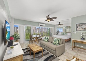 Ein modernes Wohnzimmer mit Sofa, Couchtisch und Fernseher, ein Balkon mit Essbereich und ein Schlafzimmer mit Bett und Nachttisch.