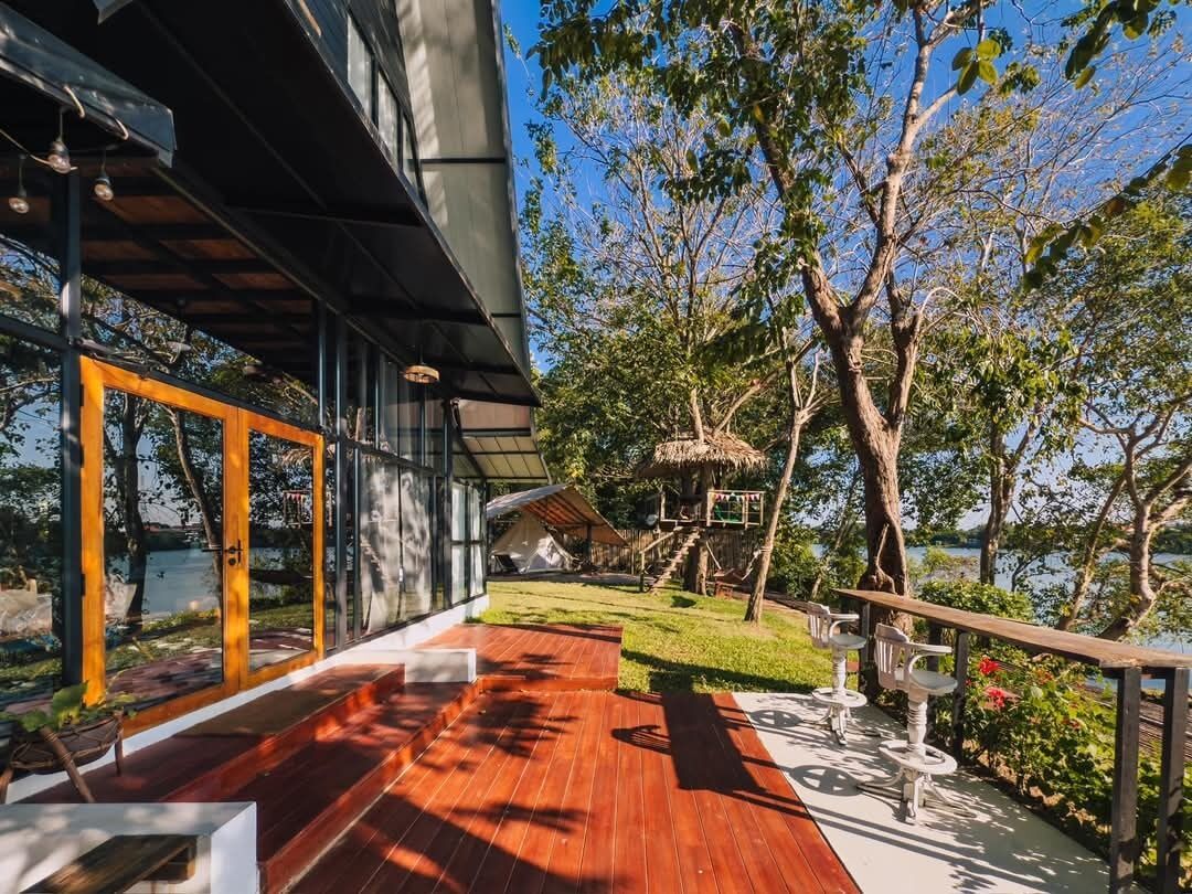 A modern building with large windows, a wooden deck, and a view of a lake.