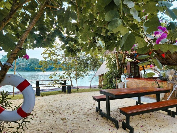 Escena junto a la playa con una mesa y bancos de madera, un flotador salvavidas y vista al agua.