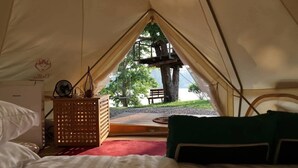 A tent with a bed, a wooden table, and a view of a tree and bench outside.