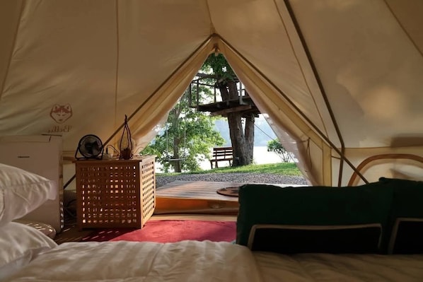 A tent with a bed, a wooden table, and a view of a tree and bench outside.