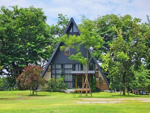 Una casa moderna con techo triangular, rodeada de vegetación exuberante y un área de picnic.