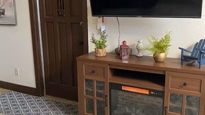 Ein Zimmer mit einem großen Flachbildfernseher, der an einem Holzkasten befestigt ist, einer Tür und einem gemusterten Teppich.