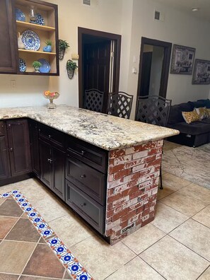A kitchen with dark cabinets, a marble countertop, and a brick accent wall. - The little house (Bakersfield)