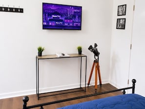 Un dormitorio con cama, escritorio con telescopio, televisor en la pared y una puerta.