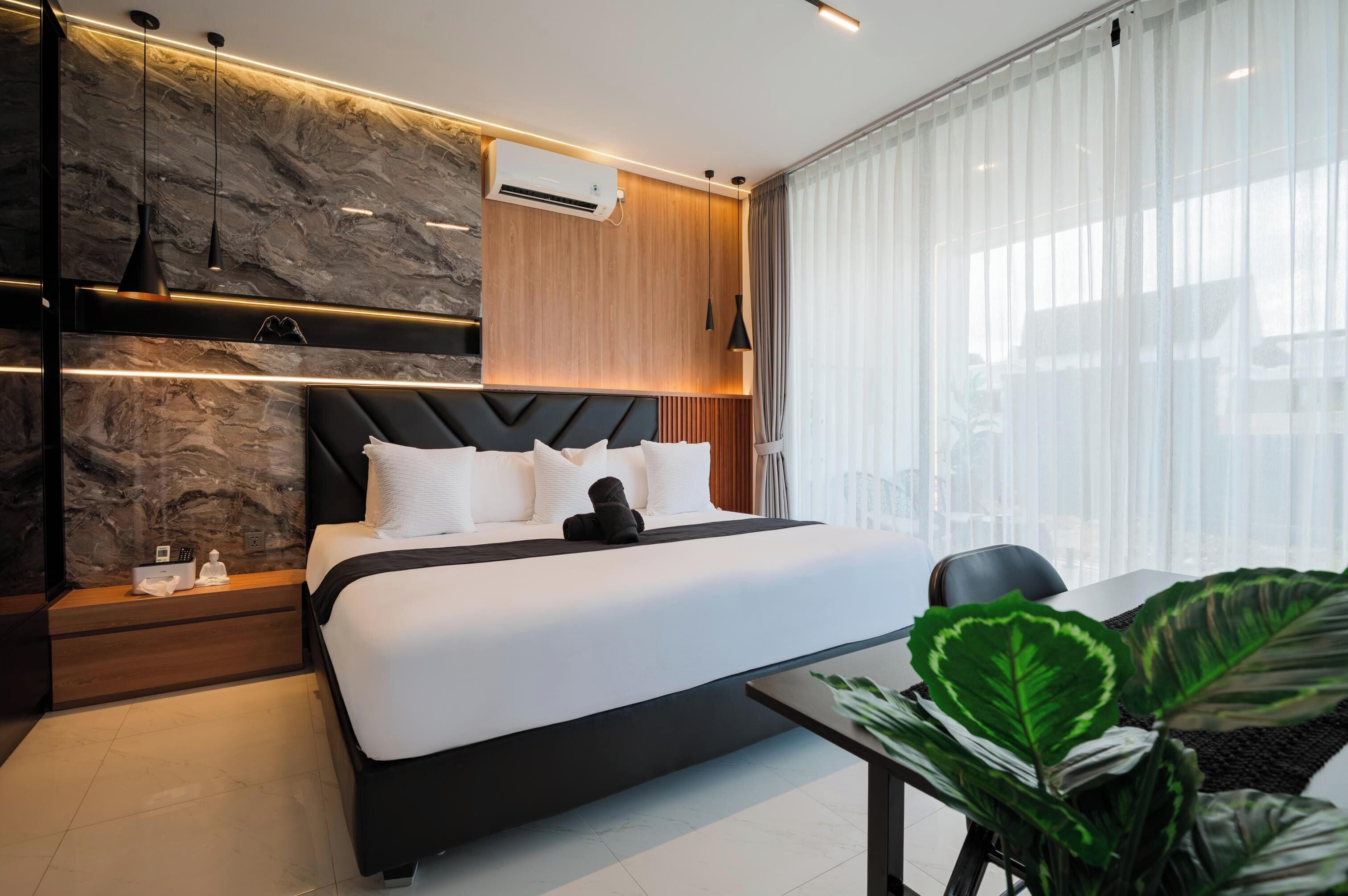 Une chambre moderne comprenant un lit, des tables de chevet, un appareil de climatisation et une grande fenêtre avec des rideaux.