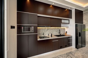 A modern kitchen with dark cabinetry, a stainless steel refrigerator, a microwave, and a granite countertop. - Sky Beach Villa by Betterplace (Canggu)
