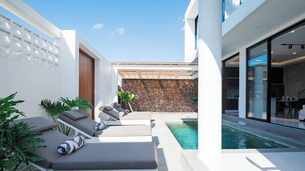 Un área de piscina moderna al aire libre con sillones de descanso, un muro de piedra y un ventanal que da a un comedor.