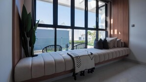 Una habitación moderna con un ventanal grande, un banco acolchado y una planta en maceta.