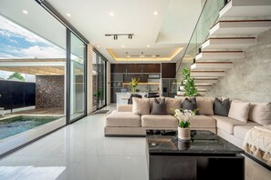 A modern living room with a large sofa, a coffee table, and a view of a swimming pool. - Sky Beach Villa by Betterplace (Canggu)