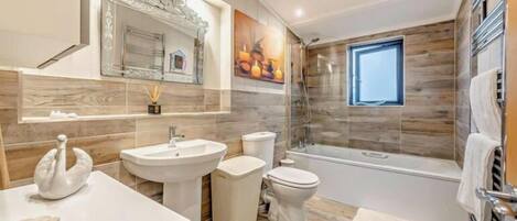 Une salle de bain moderne dotée d’une grande baignoire, de toilettes séparées et d’un meuble-lavabo avec un miroir.