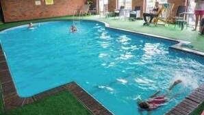 Una piscina interna con parete in mattoni, prato sintetico verde e poltrone relax.