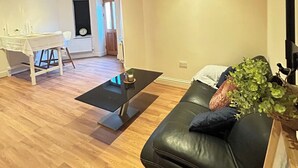 Un salon avec un canapé en cuir noir, une table basse en verre, une table à manger avec des chaises et une plante posée sur le canapé.