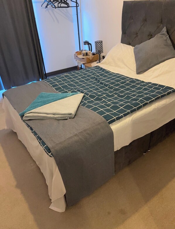 Ein ordentlich bezogenes Bett mit einer gemusterten Tagesdecke, einer grauen Zudecke und einem passenden Kissen.