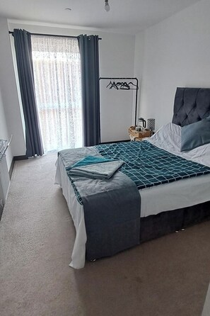 Ein Schlafzimmer mit einem Bett, einem Nachttisch mit Lampe, einem Heizkörper und einem Fenster mit Vorhängen.