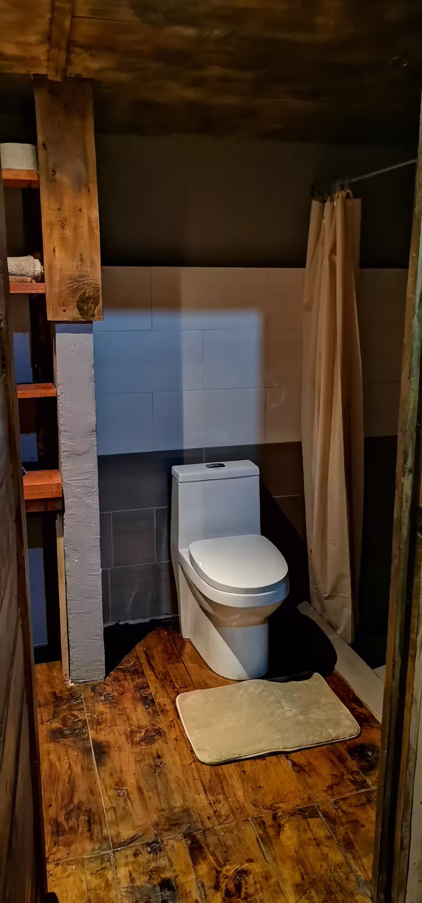 Ein kleines Badezimmer mit Toilette, Holzboden, einer weißen Matte und einer Duschvorhang.