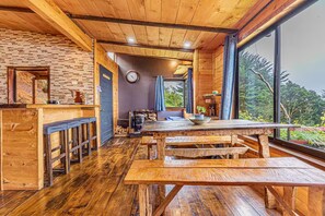 A rustic wooden interior with a large dining table, benches, a brick wall, and a view through large windows. - Jaulares Country House (Rivas)