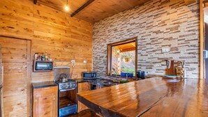A rustic kitchen with wooden walls, a stone wall backsplash, and a large wooden bar counter. - Jaulares Country House (Rivas)