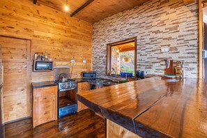 A rustic kitchen with wooden walls, a stone wall backsplash, and a large wooden bar counter. - Jaulares Country House (Rivas)