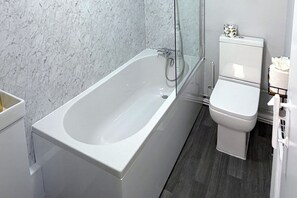 A bathroom with a white bathtub, a toilet, and a marble wall. - Central Hull, 3Br Contractors & Street Parking (Hull)