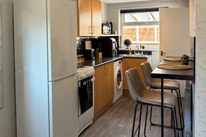 A compact kitchen with a refrigerator, oven, microwave, and washing machine. There is a small dining area with a table and chairs. - Central Hull, 3Br Contractors & Street Parking (Hull)
