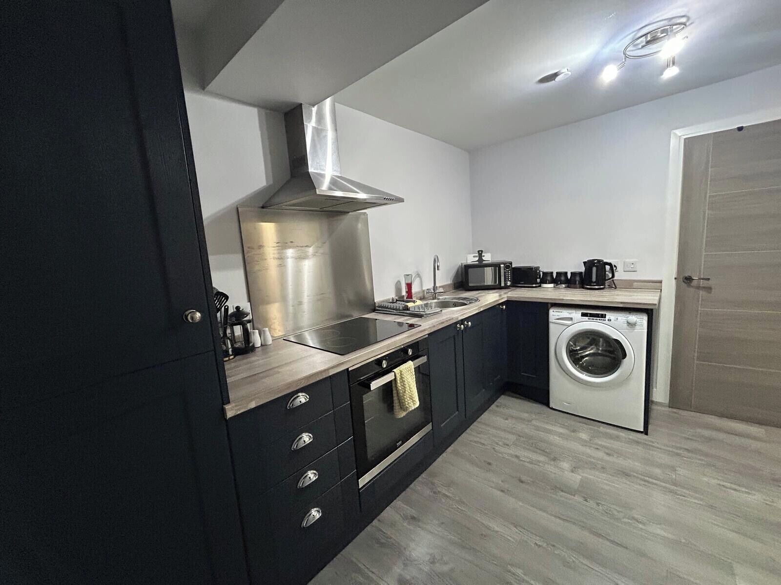 Een praktische keuken met een roestvrijstalen afzuigkap, een ingebouwde magnetron, een wasmachine en een spoelbak.