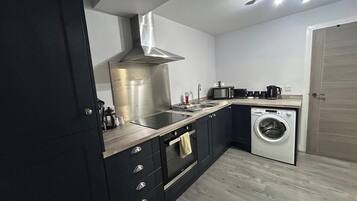 Een praktische keuken met een roestvrijstalen afzuigkap, een ingebouwde magnetron, een wasmachine en een spoelbak.