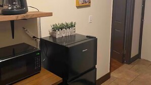 Una cocina con cafetera, microondas, refrigerador y dos cuadros en la pared.