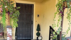 Una escalera de hormigón que conduce a una puerta con barandilla de metal, una pequeña planta en maceta y un felpudo.
