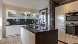 Una cocina moderna con armarios blancos, una isla central, horno empotrado y una pared decorativa de piedra.