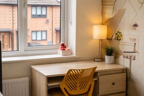 Una habitación con un escritorio de madera, una silla, una lámpara, una planta en maceta y un piano.
