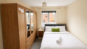 Camera da letto con un letto, un armadio in legno, uno specchio, un comodino, una lampada e una finestra.