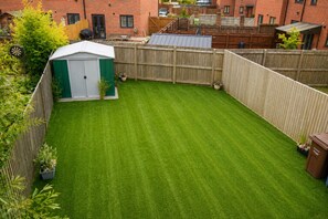 Un patio trasero con césped verde, un cobertizo y una valla de madera.