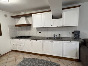A kitchen with white cabinets, a gas stove, a sink, and a coffee maker. - Vrbo Property (Porto Frailis)