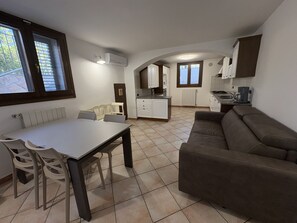 A compact living space with a dining area, a sofa, a kitchen, and a window with blinds. - Vrbo Property (Porto Frailis)