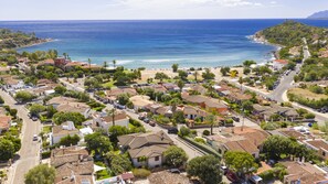 Luftaufnahme einer Küstenstadt mit Häusern mit Terrakotta-Dächern, einem Strand und einem klaren, blauen Meer.