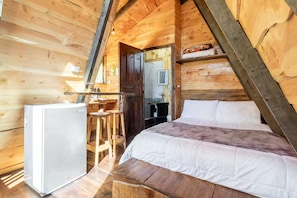 A wooden cabin with a bed, a small kitchenette, and a wooden stool.