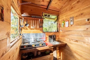 A compact wooden cabin kitchen with a stove, sink, and hanging utensils.
